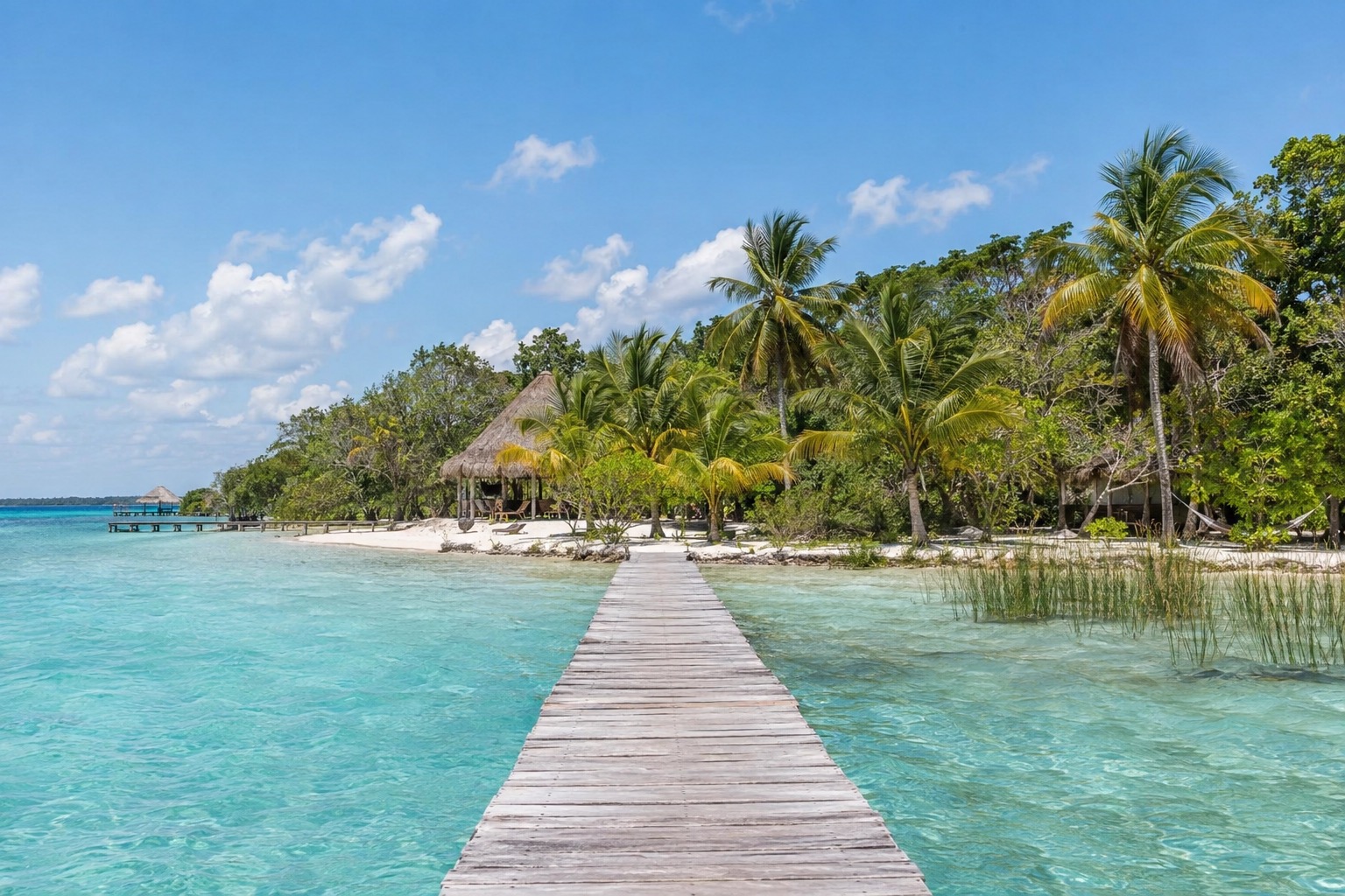 Wooden dock reaching into turquoise lagoon water with a low green shoreline behind it at Bacalar, Mexico