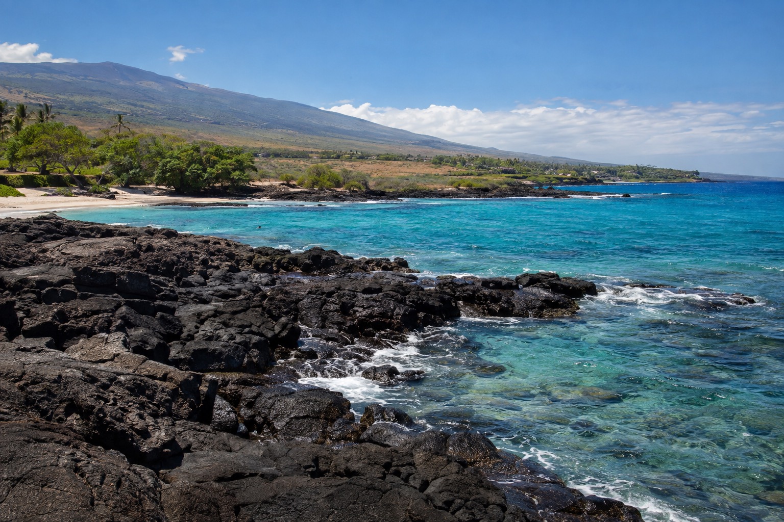A resort beach along Hawaii's dry Kona coast with black lava rock in the foreground