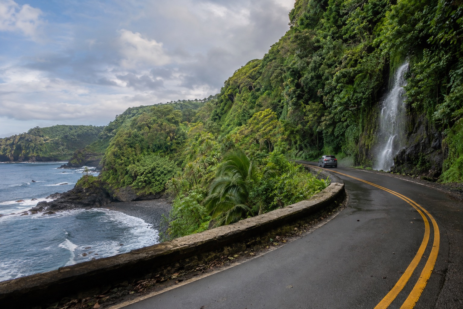 A narrow two-lane highway curving through rainforest on Maui's northeast coast