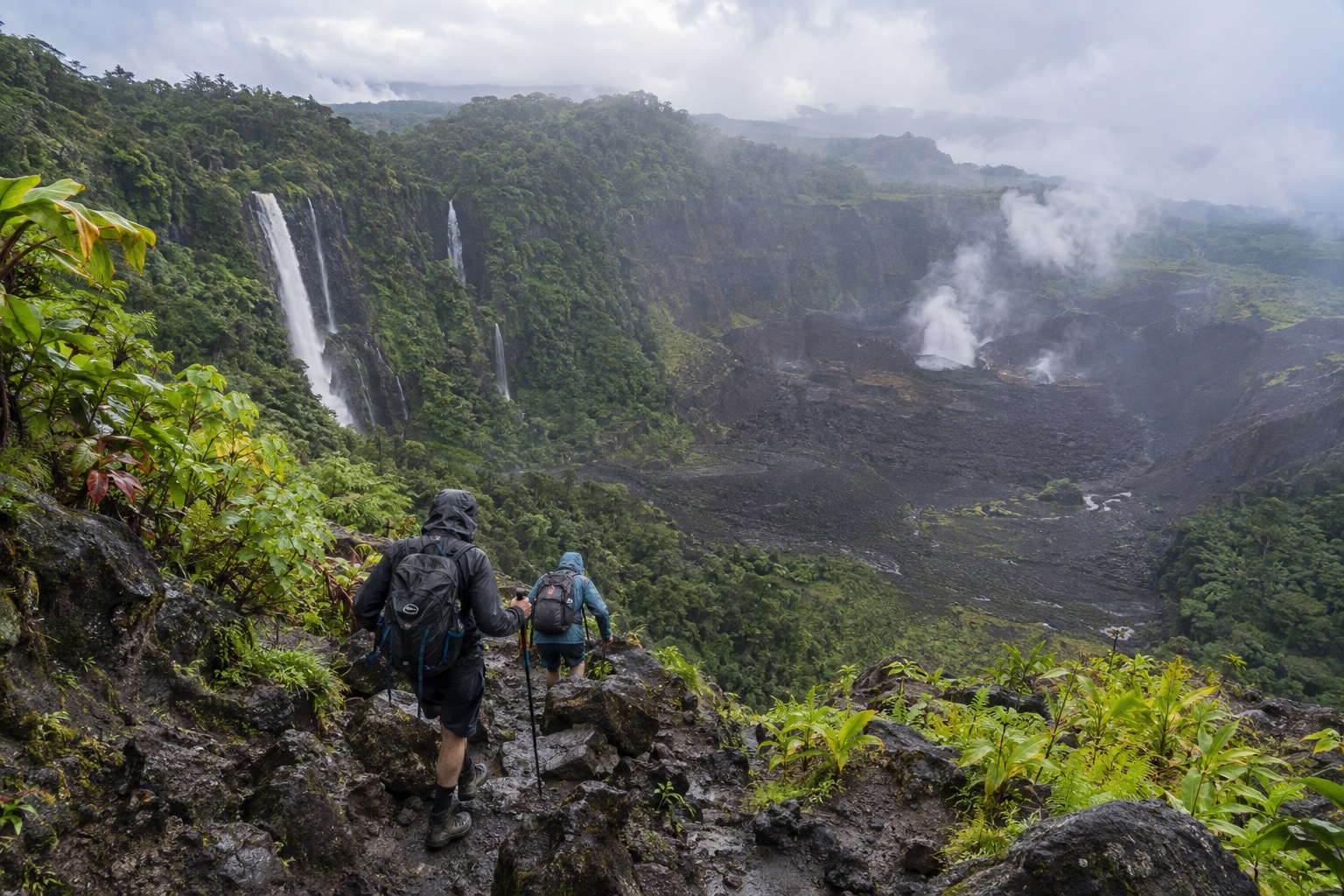 Hikers descending a steep rocky path into a large volcanic crater
