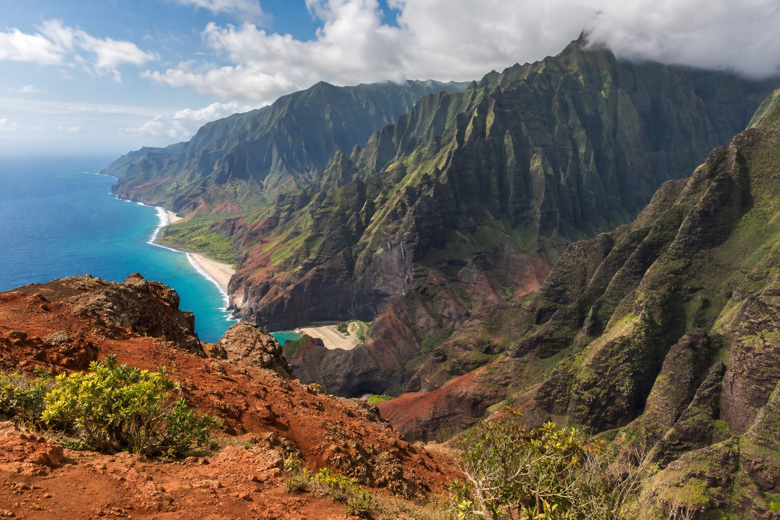 A red-rock canyon with layered cliffs and green ridgelines under a partly cloudy sky
