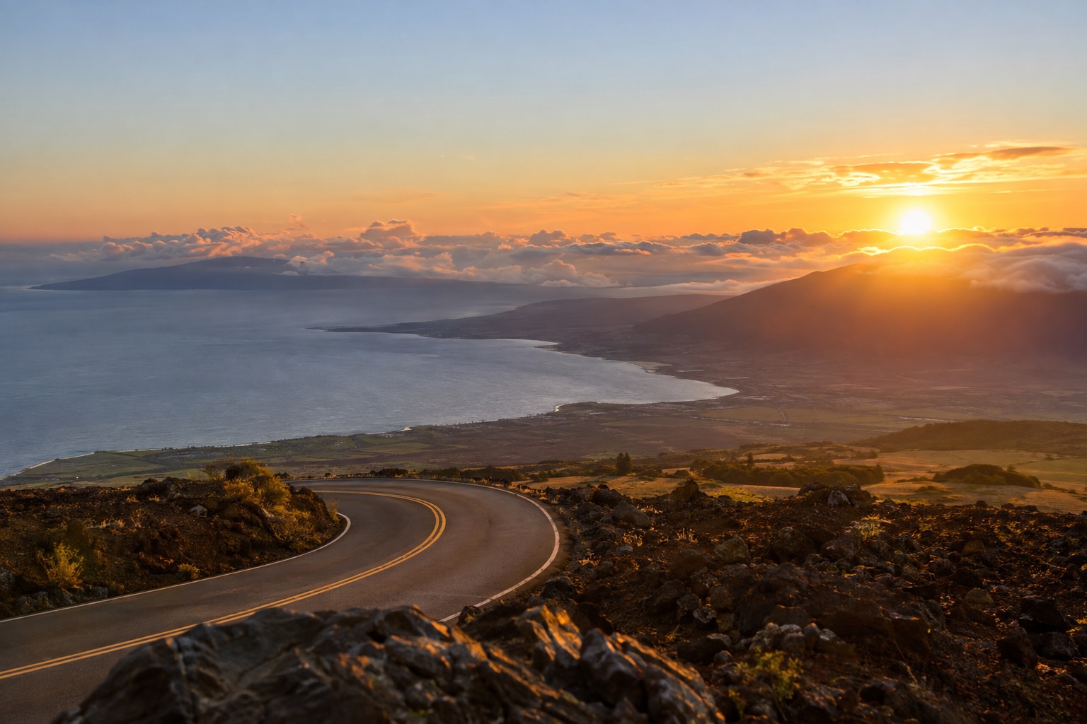 Sunrise light over a sea of clouds seen from a volcanic summit road on Maui