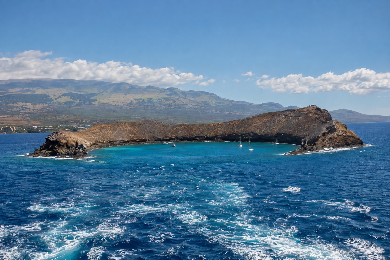 A crescent-shaped volcanic islet surrounded by clear turquoise water off Maui's coast, seen from a boat