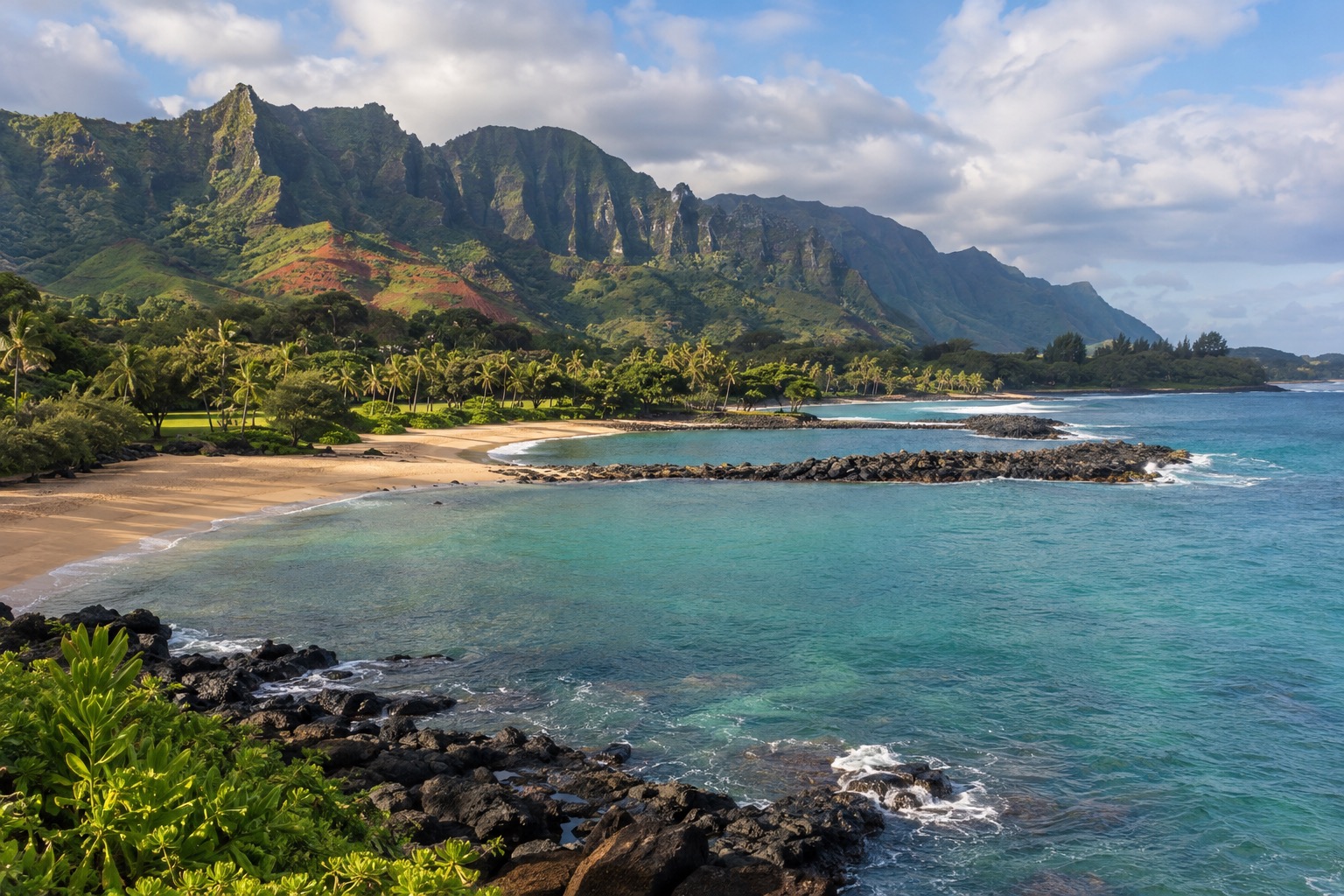 A crescent beach in Poipu split by a stone breakwater, with lava rock at each end