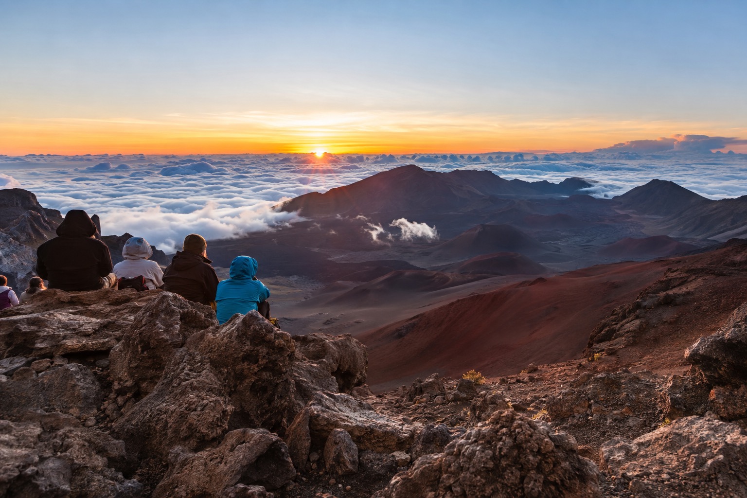 Clouds below the summit of Haleakala at first light, with visitors in jackets watching the horizon