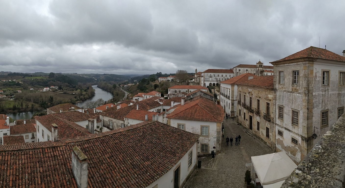 Stone university buildings on the hill above Coimbra under low gray cloud, with tiled rooftops below