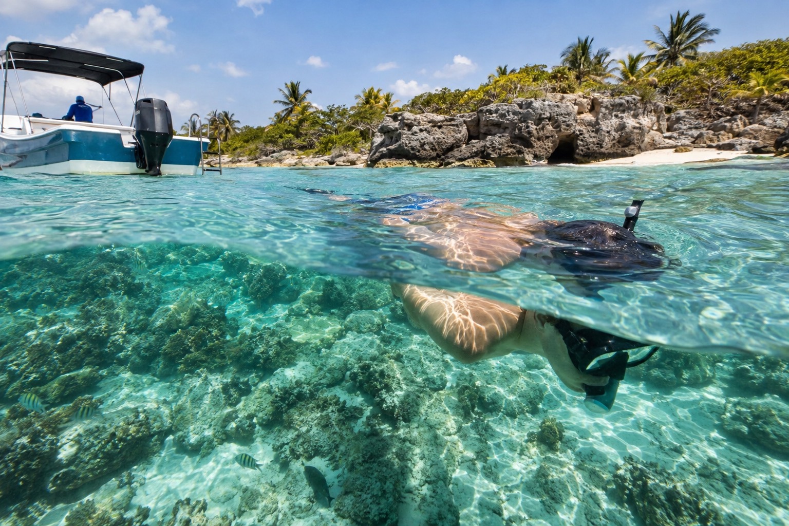 A snorkeler floating above a coral reef in clear turquoise water near a boat