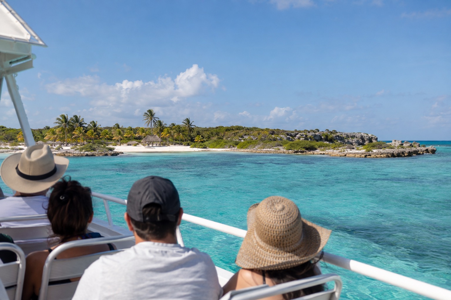 A passenger ferry crossing turquoise Caribbean water toward a low island shoreline