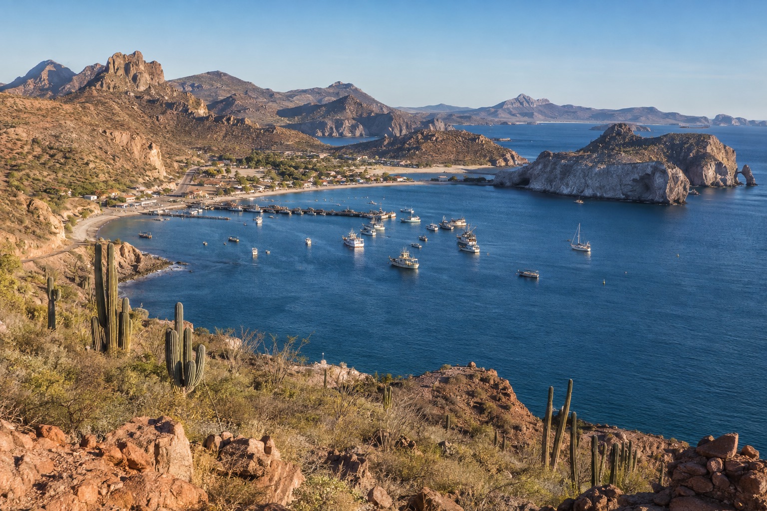 A curved bay with a working harbor and low hills behind it on a clear spring morning