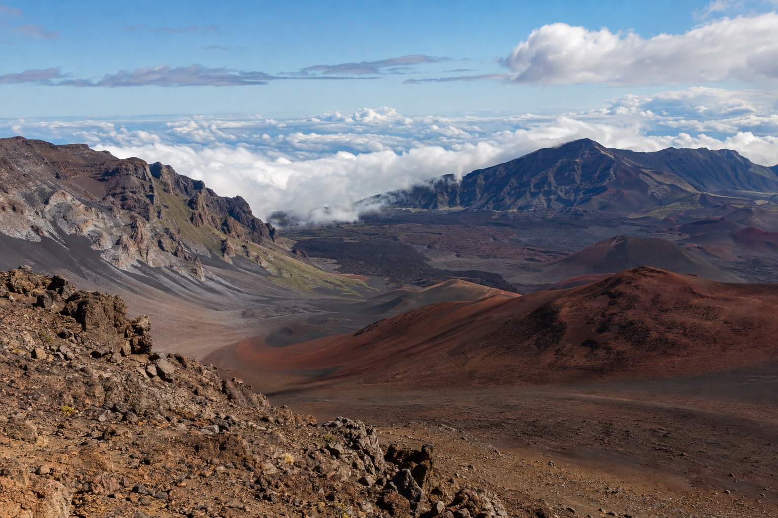 Reddish and black cinder cones inside Haleakala's summit crater under a partly cloudy sky