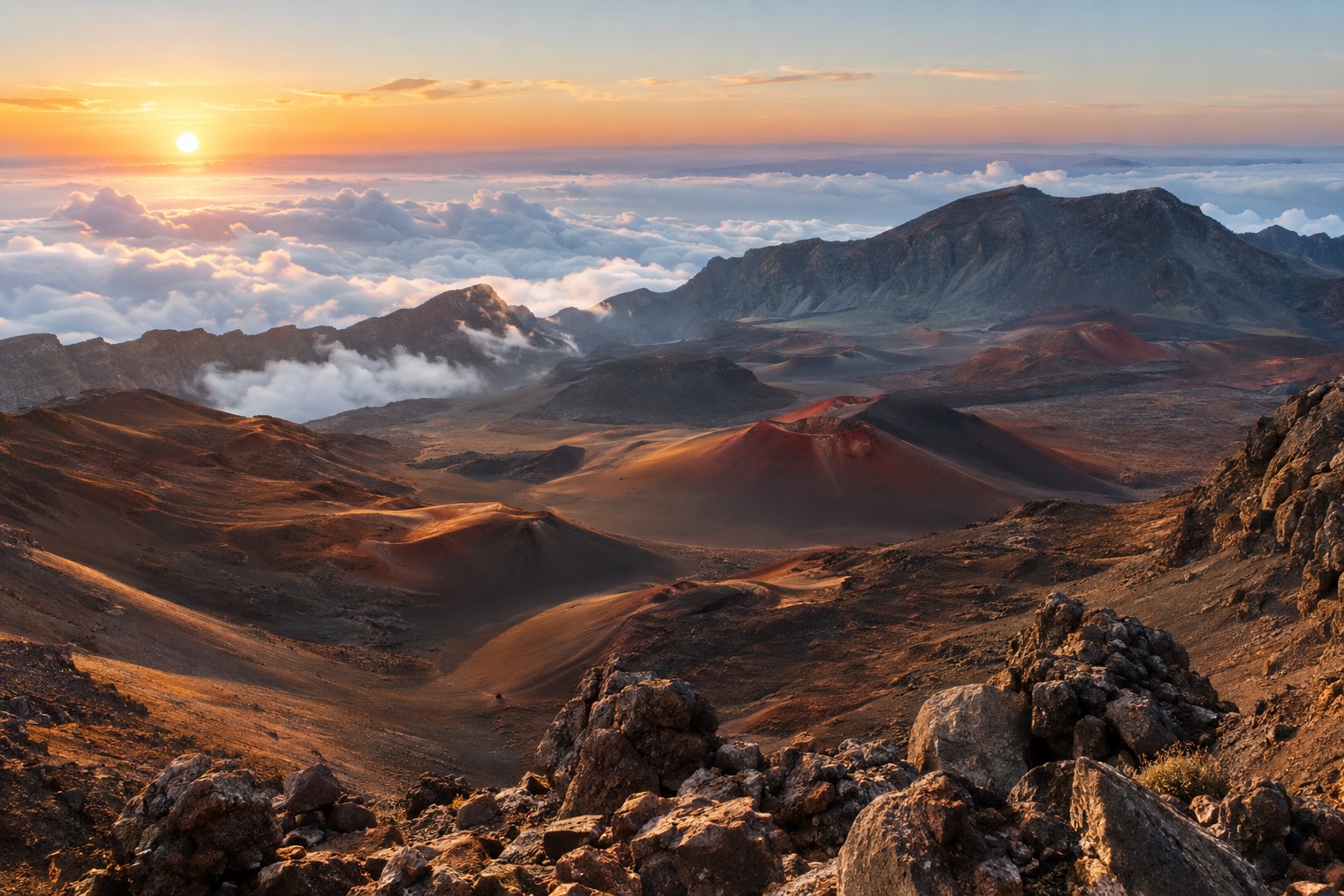 Red and black cinder cones inside the Haleakala crater at sunrise, with clouds pooling below the rim