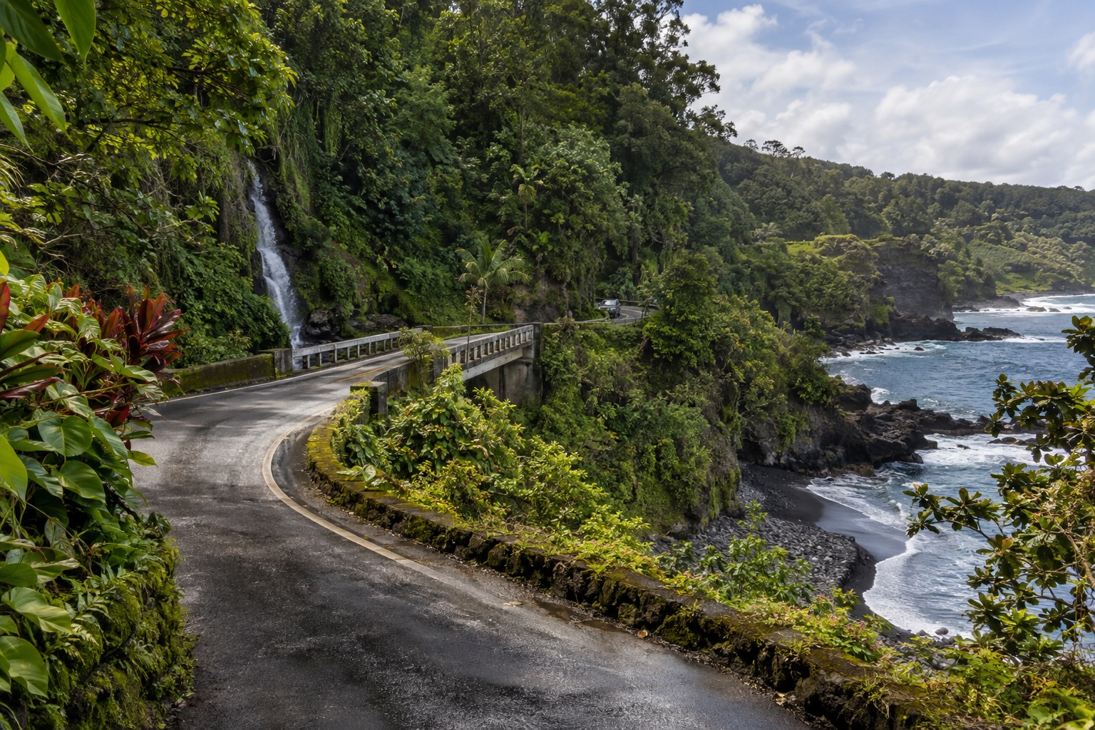 A stretch of the Hana Highway curving through rainforest toward a one-lane bridge