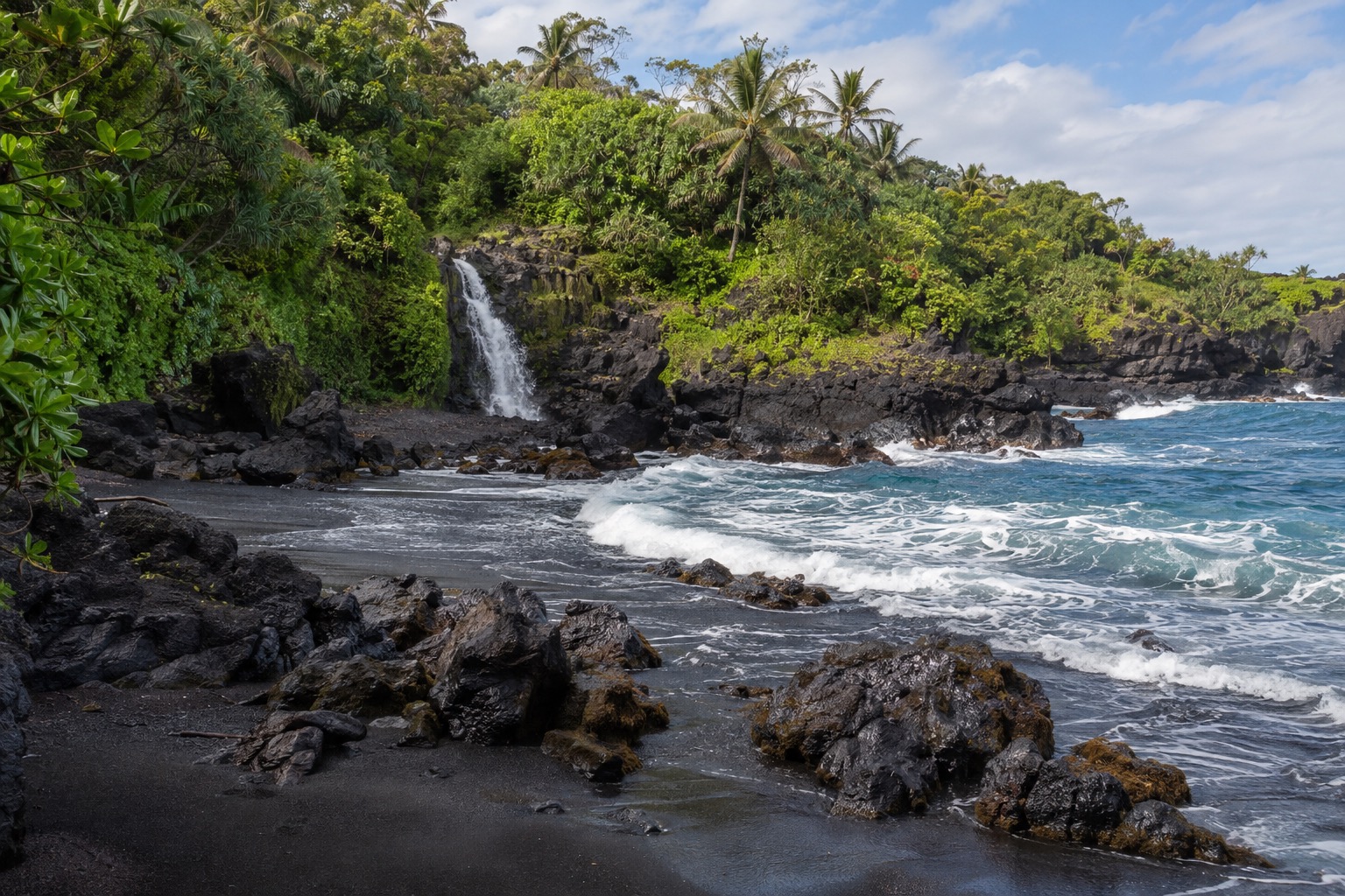 A black sand beach with lava rock outcrops along Maui's Hana coast