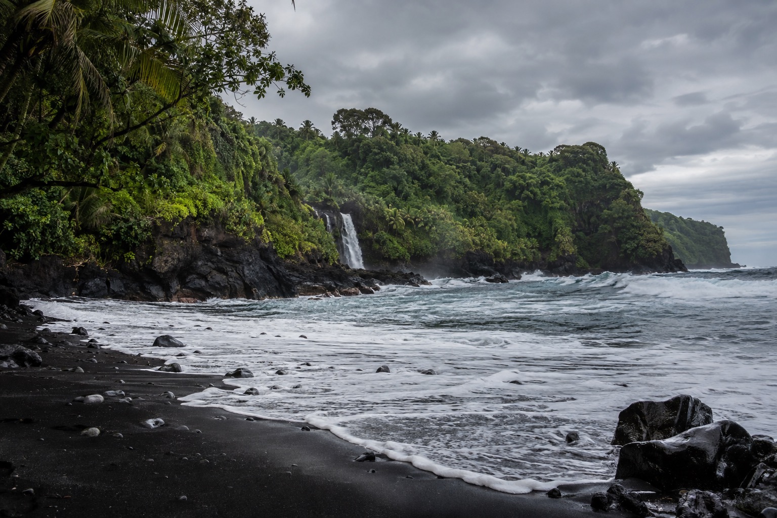 Waves breaking on black volcanic sand under an overcast winter sky