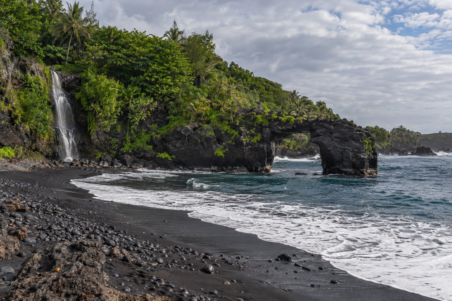Black sand beach with a natural stone arch at a coastal state park