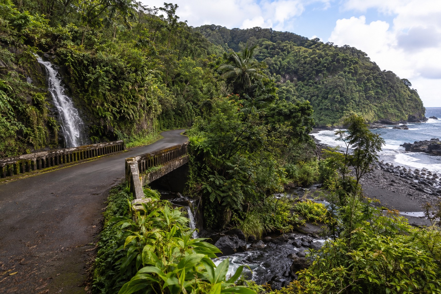 A narrow highway bridge crossing a stream lined with tropical foliage on Maui's east coast