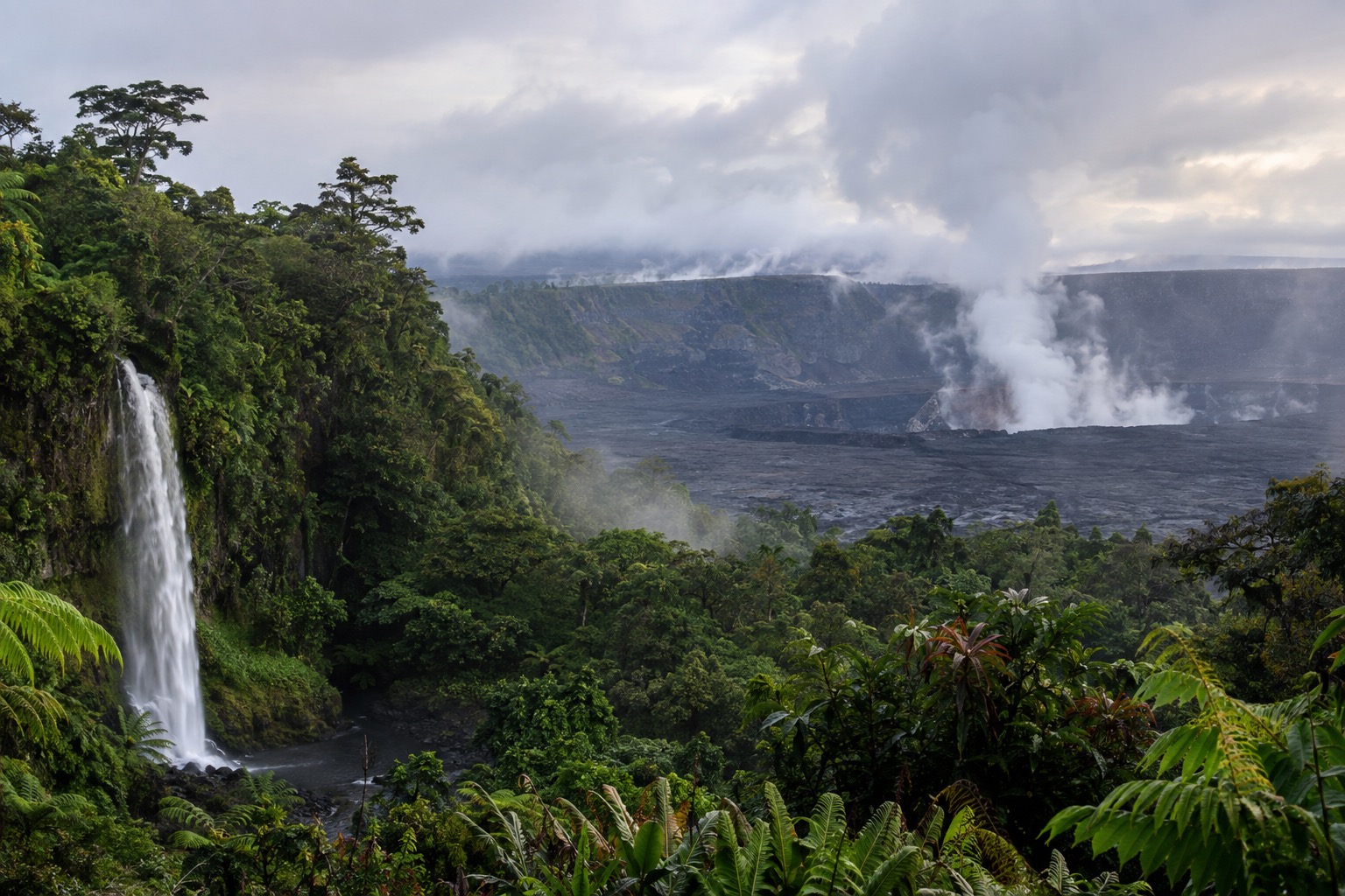 Steam rising from a volcanic crater with fog and green vegetation along the rim on a cool morning