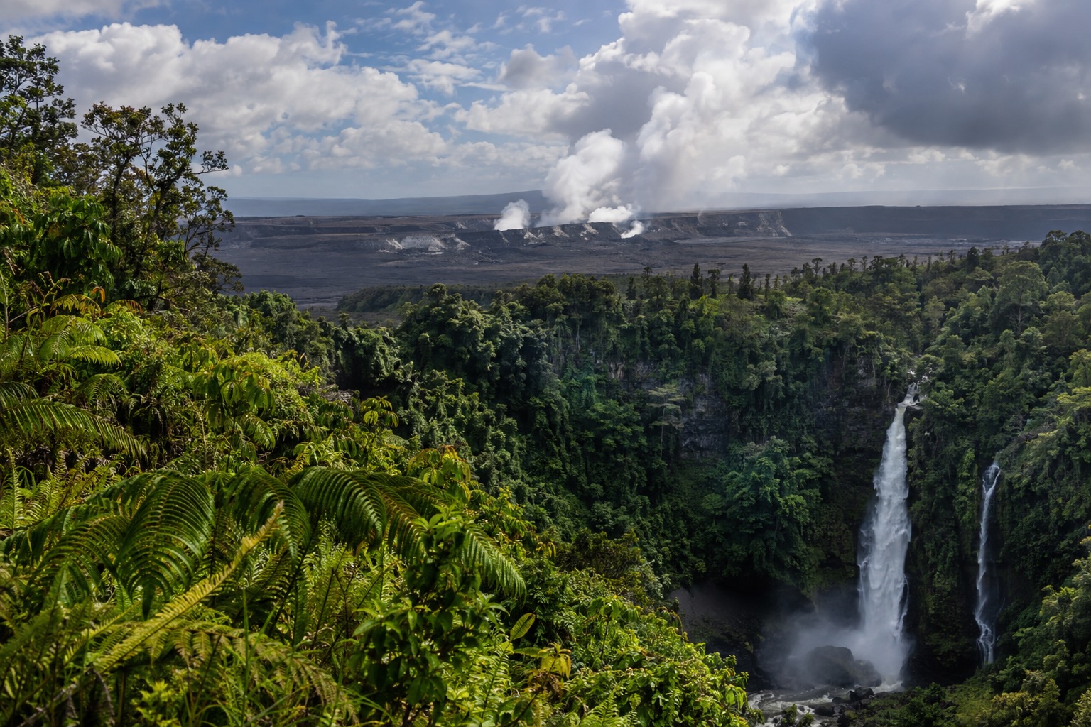 Steam rising from vents at the Kilauea summit under a partly cloudy sky
