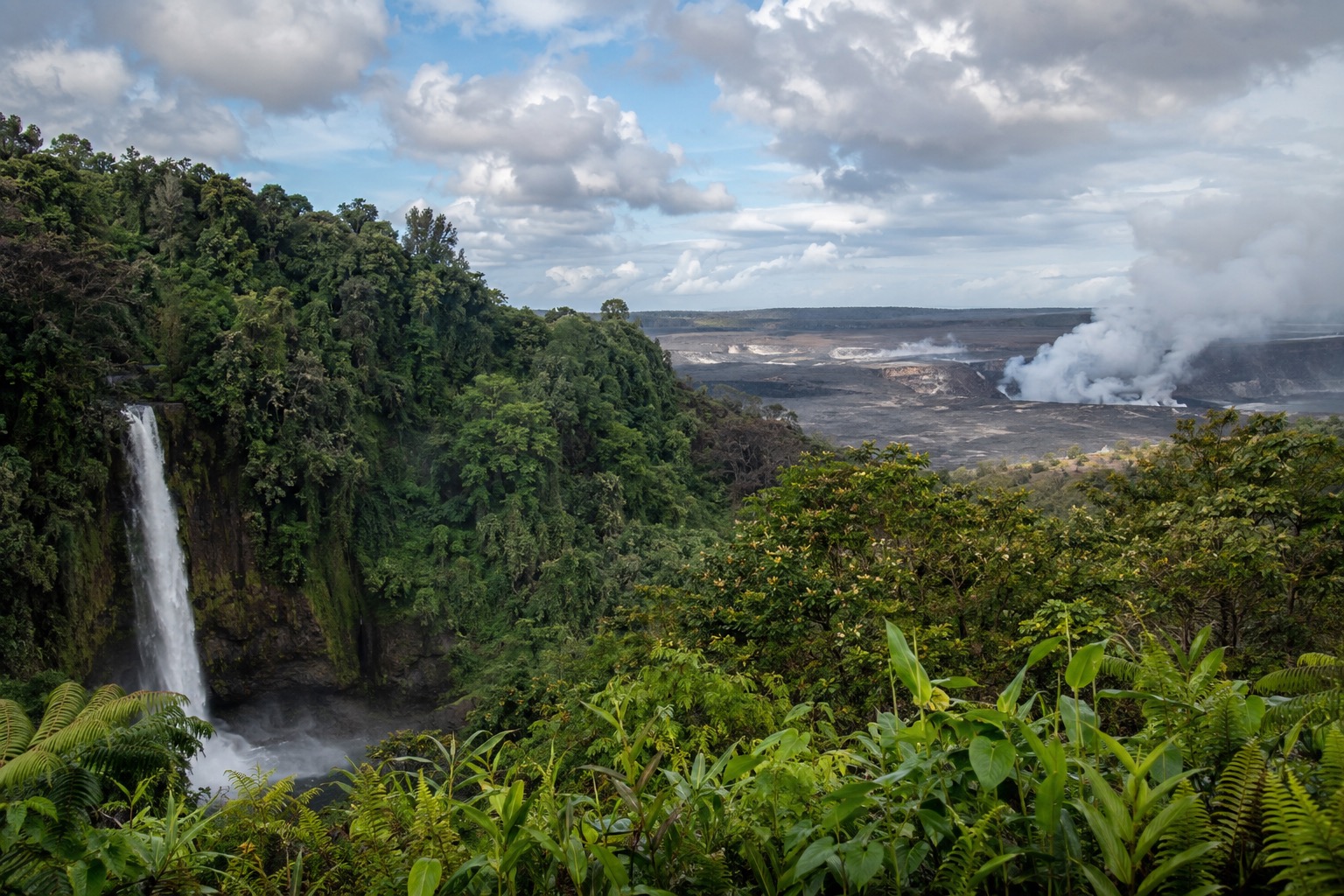 Steam rising from a crater at Hawaii Volcanoes National Park under a partly cloudy sky