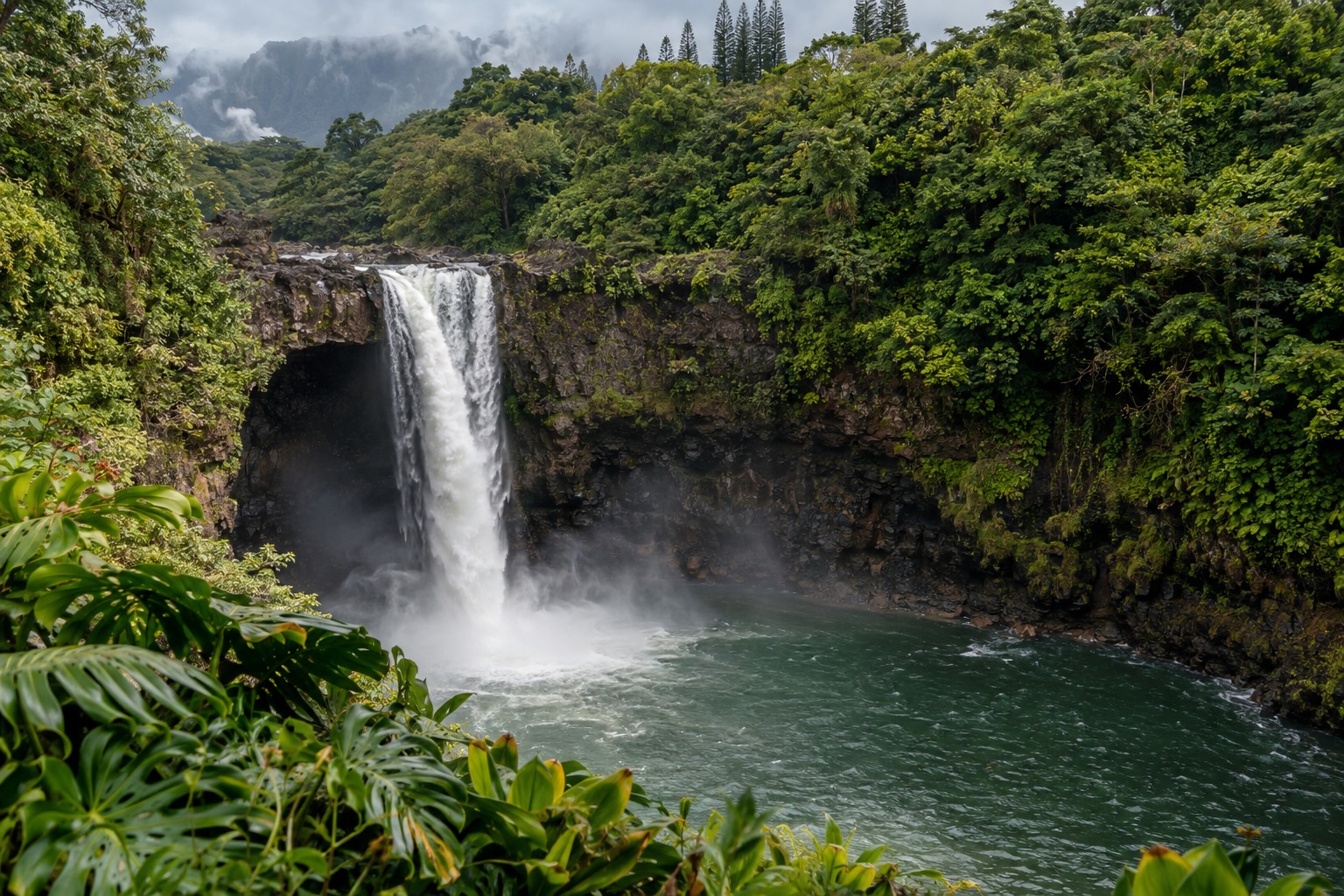 Waiānuenue Rainbow Falls dropping into a green pool surrounded by jungle in Hilo, Hawaii