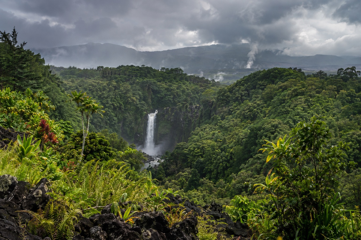 Rain clouds over green hills near Hilo, Hawaii, with a waterfall visible in the distance