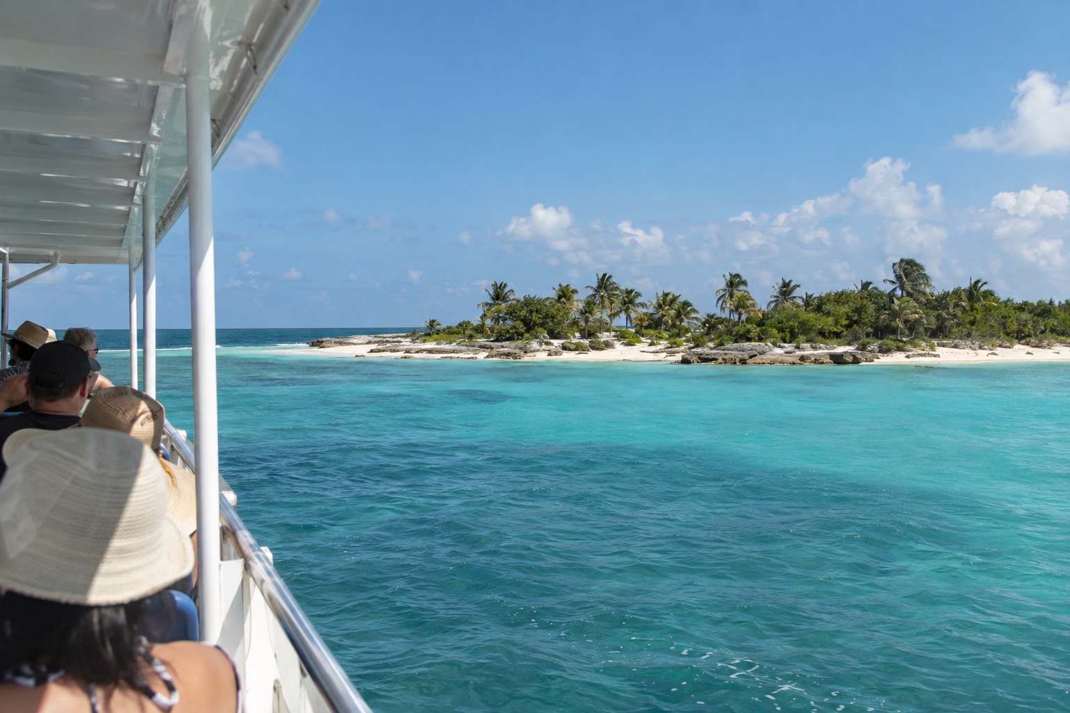 A passenger ferry approaching a low Caribbean island with turquoise shallows and a pale beach