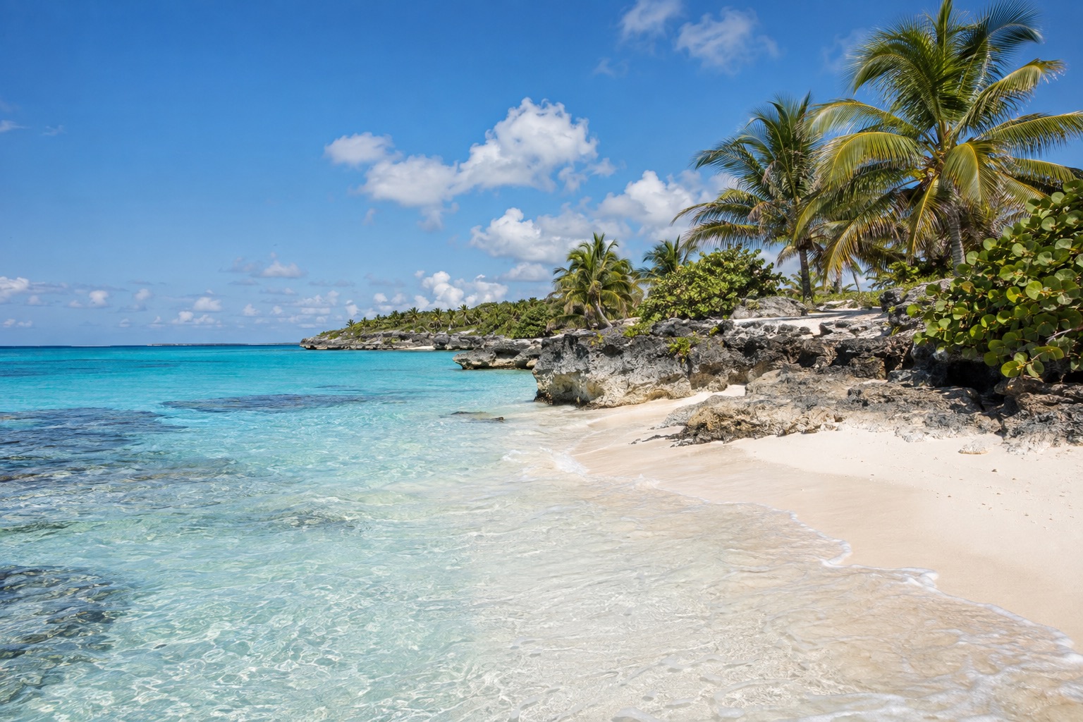 Turquoise shallow water and pale sand on a small Caribbean island under a bright sky