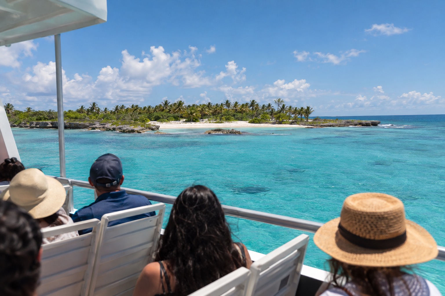 A passenger ferry crossing a turquoise channel toward a low tropical island