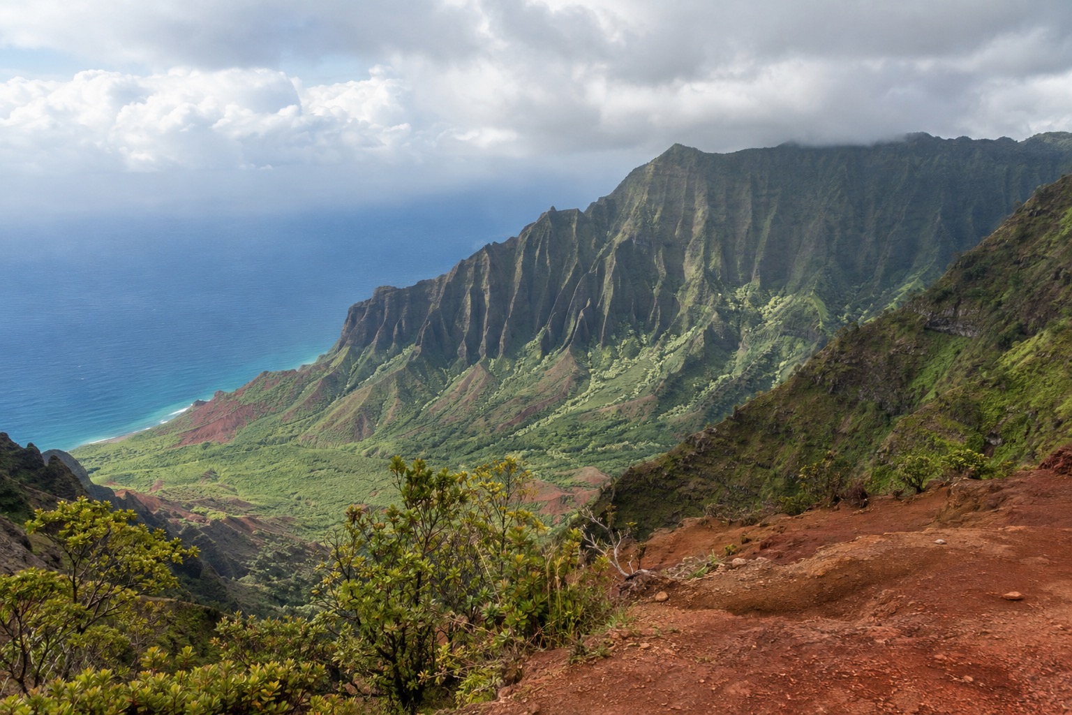 A canyon overlook with layered red and green rock walls under a cloudy sky