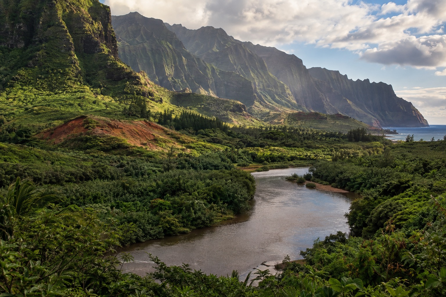 A river winding through a forested valley on Kauai's east side, with green cliffs behind