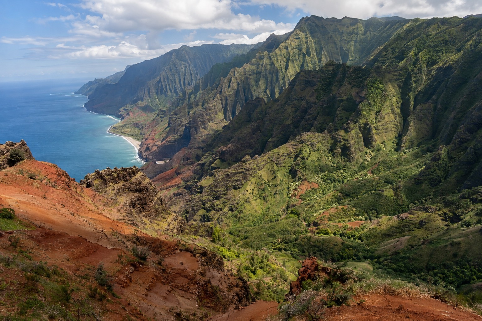 A wide canyon with layered red and green rock walls under a partly cloudy sky