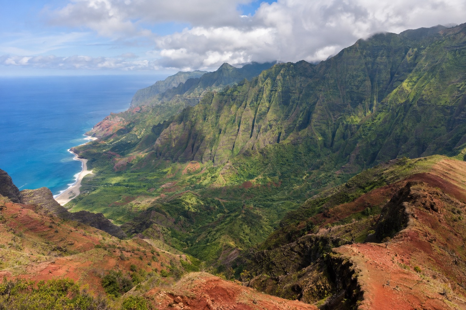 A steep canyon with layered red and green rock walls under a partly cloudy sky