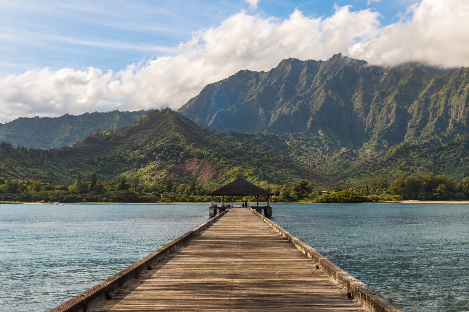 Wooden pier reaching into a calm bay with green mountains behind it