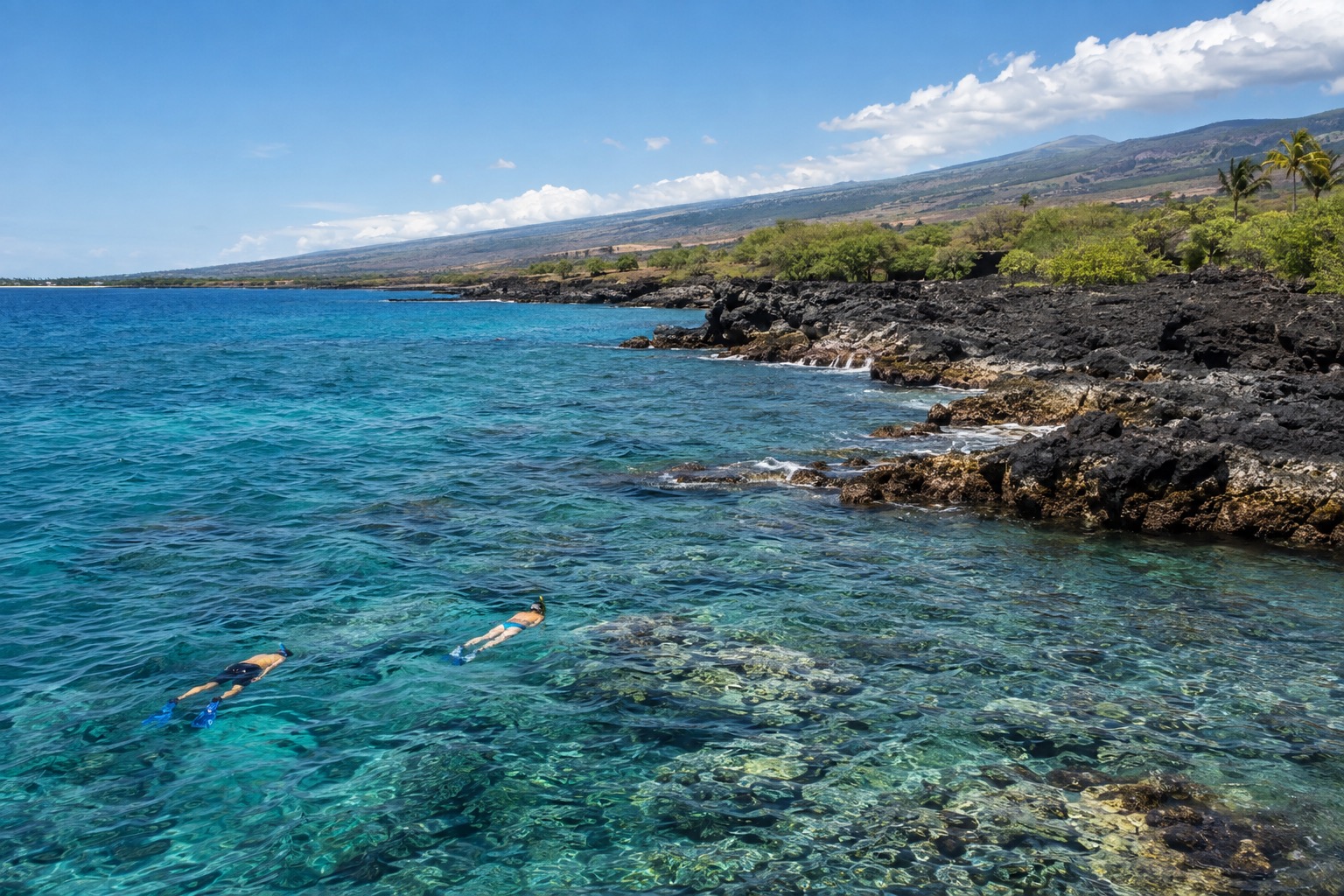 Snorkelers swimming over coral near a rocky Kona shoreline under bright midday sun