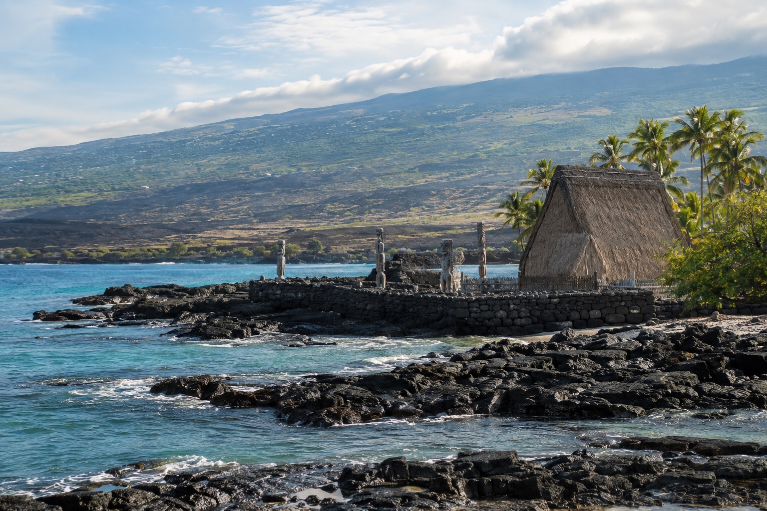 Stone platforms and thatched structures at a historic Hawaiian sanctuary site near the shoreline