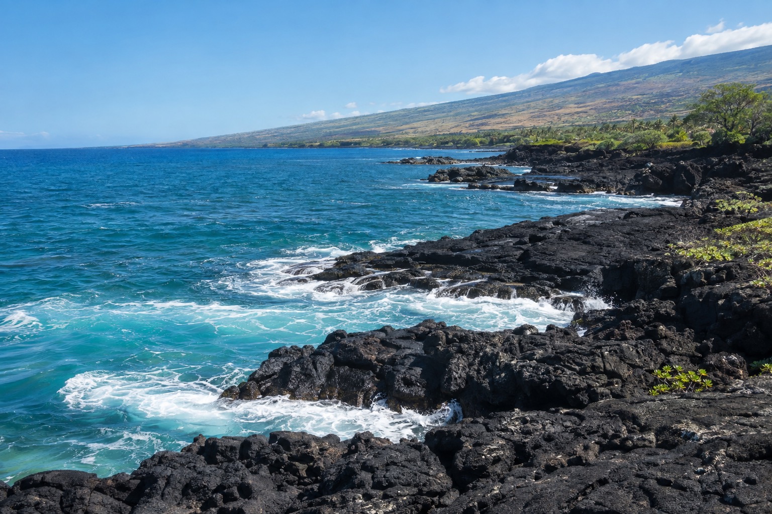 Waves breaking on a black lava rock shoreline near Kailua-Kona under a clear afternoon sky