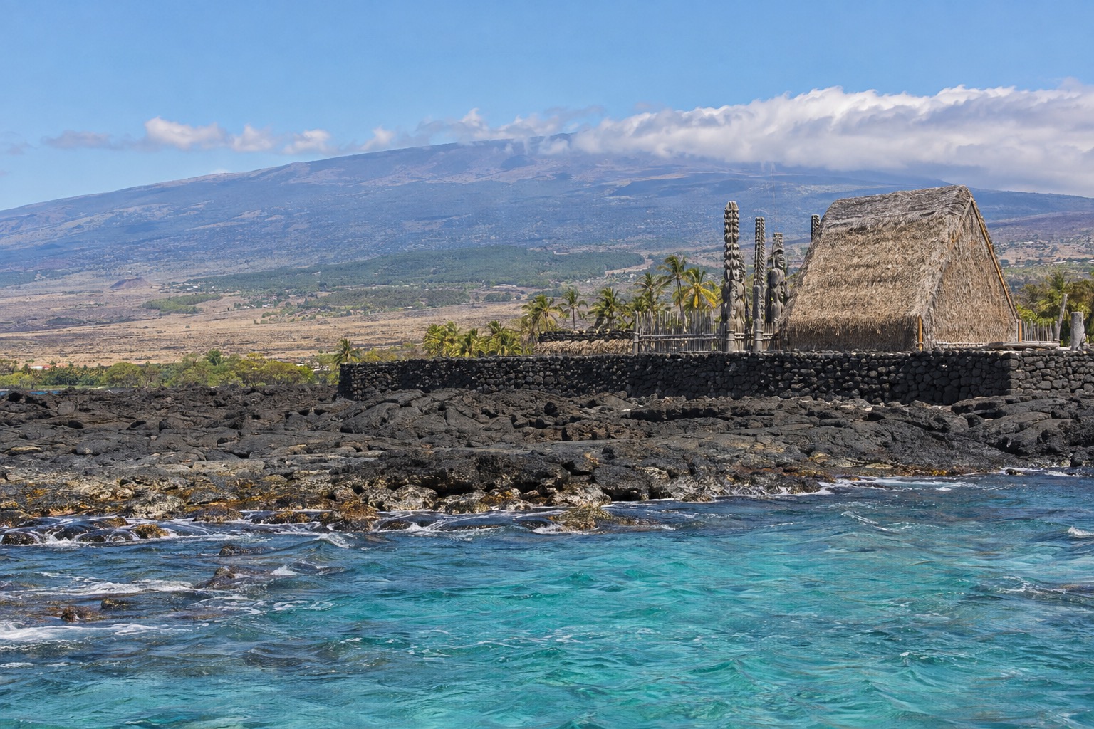 Stone wall and thatched structures at a Hawaiian historical park along the Kona coast