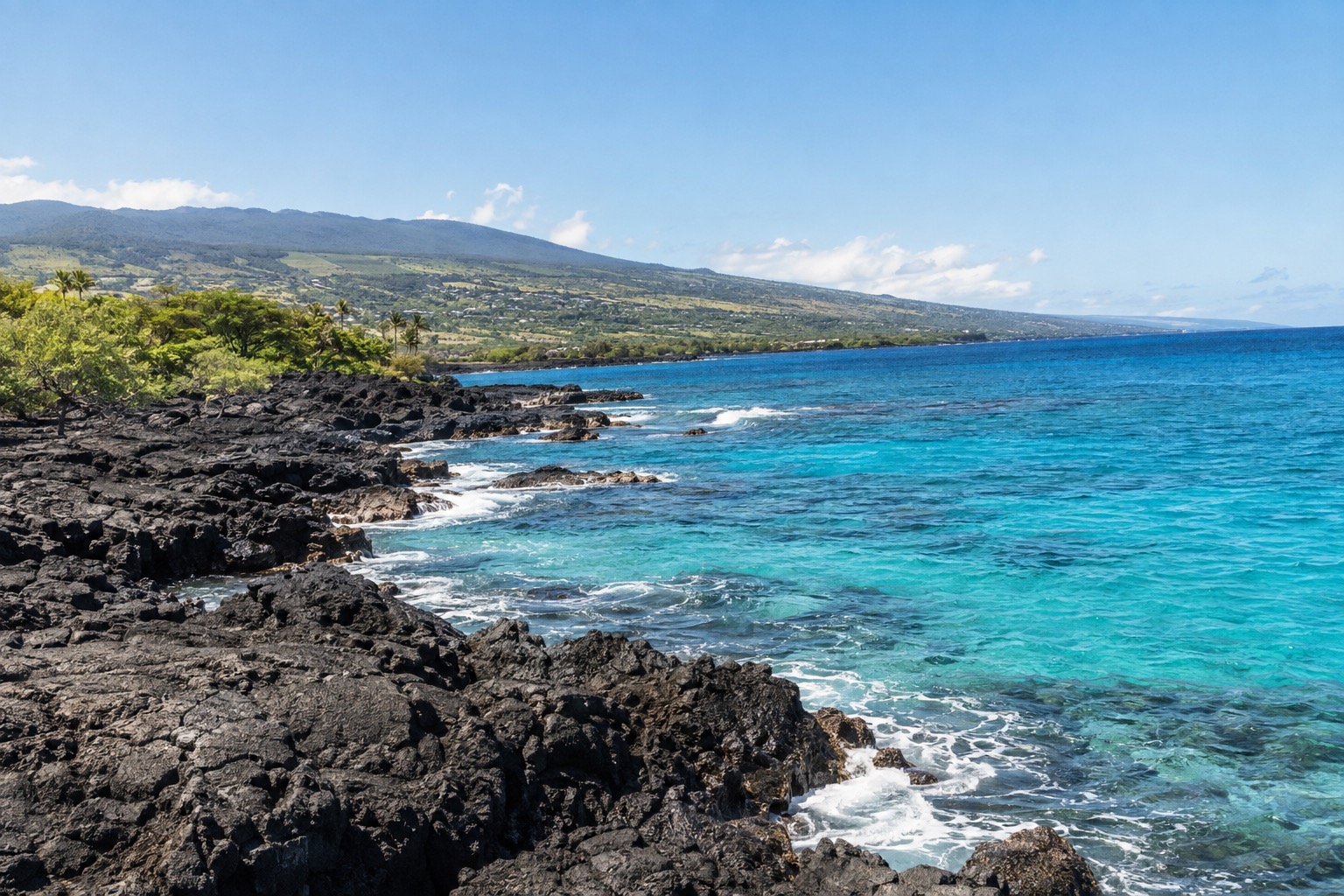 A rugged black lava shoreline meeting turquoise water under a clear midday sky near Kailua-Kona