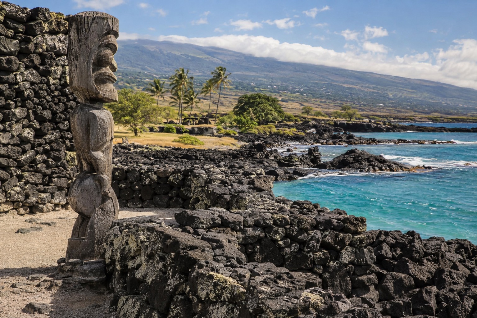 Stone temple walls and a carved wooden figure at a coastal historical park on the Kona coast