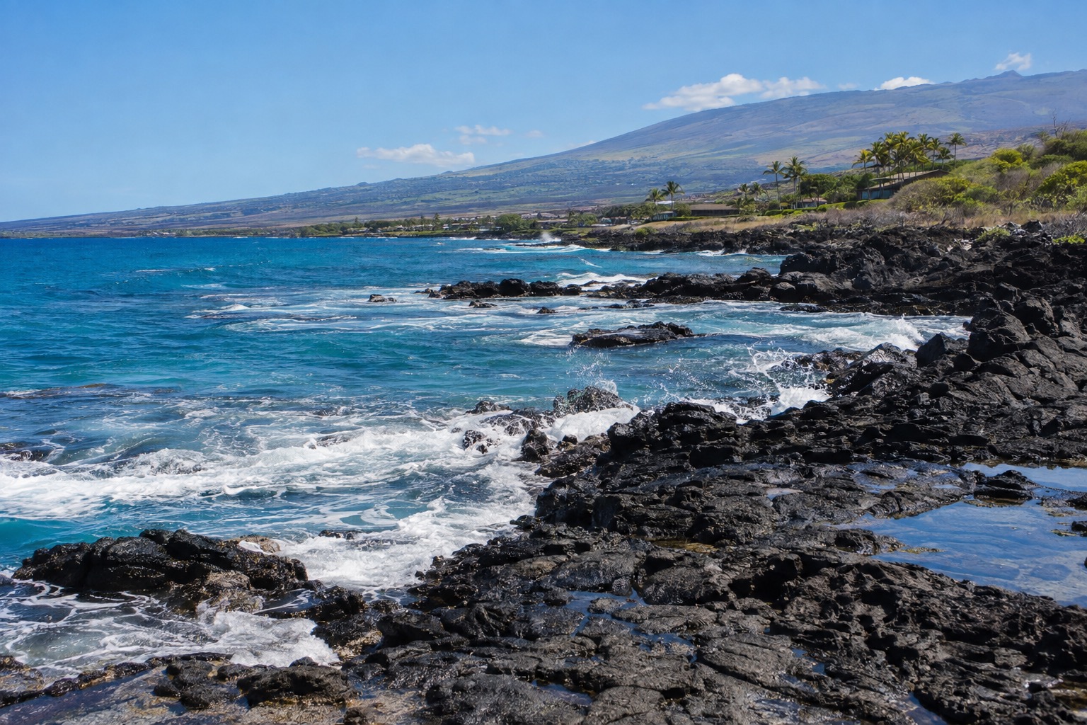 Waves breaking on a black lava-rock shoreline near Kailua-Kona under a clear sky