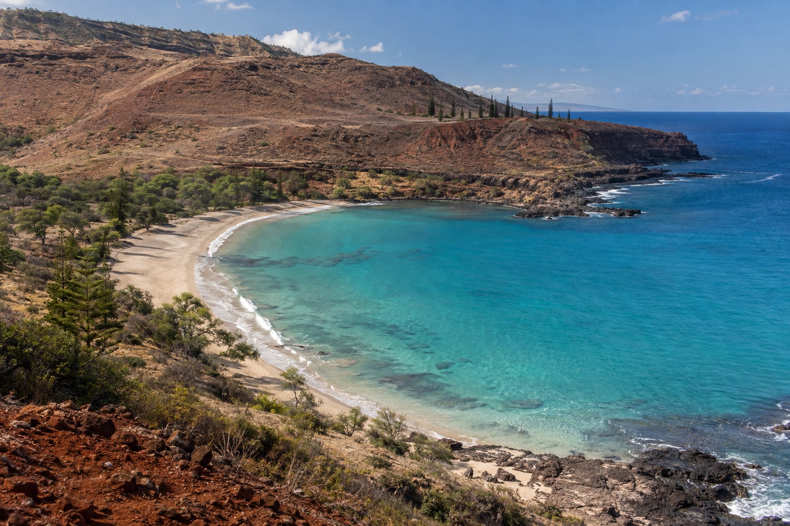 Turquoise water and a crescent of sand at a bay on Lanai's south shore, with dry hills rising behind