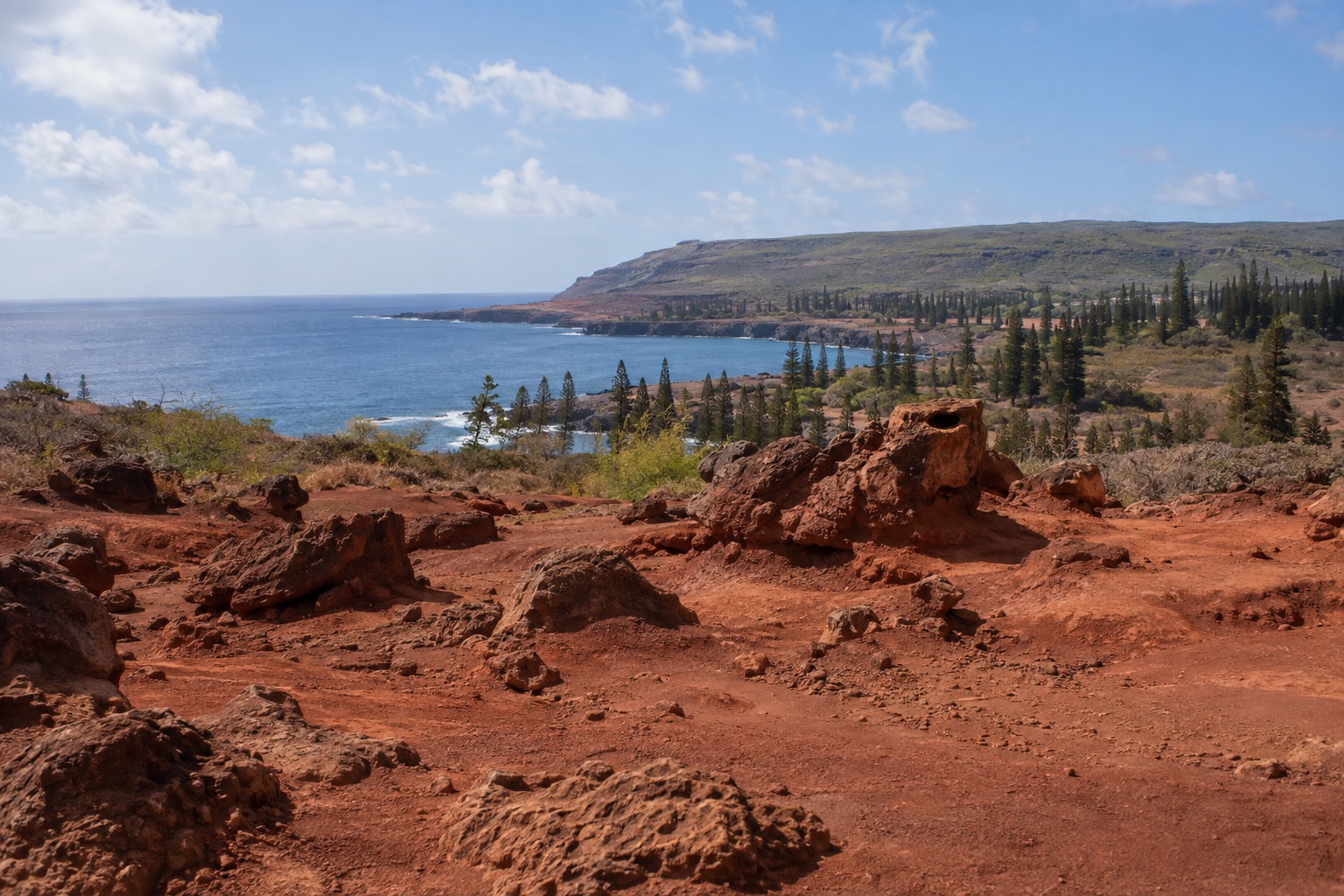 A dry, reddish dirt landscape scattered with wind-shaped rock formations under an open sky