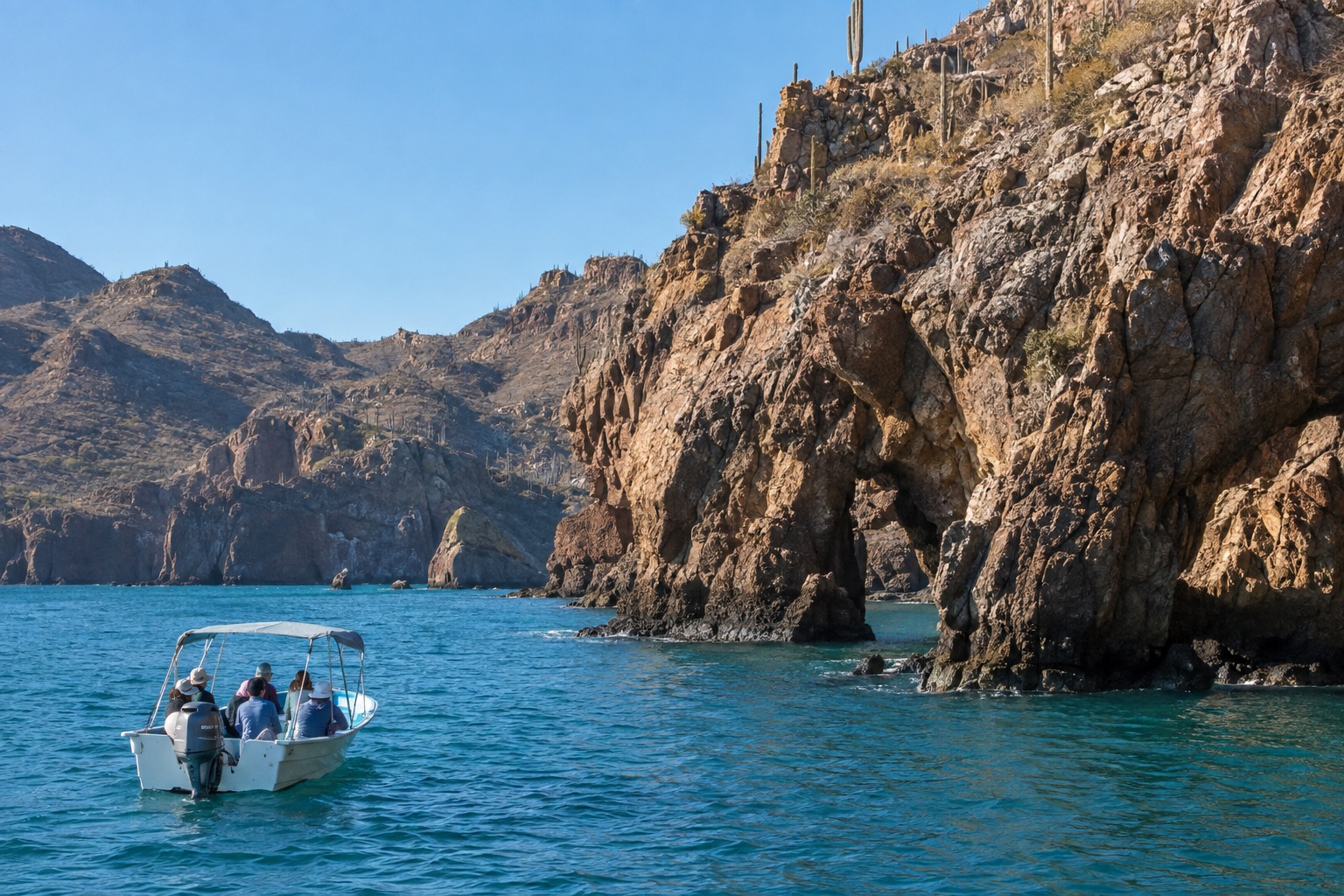 Small tour boat on turquoise bay water beside a rocky island under a clear sky