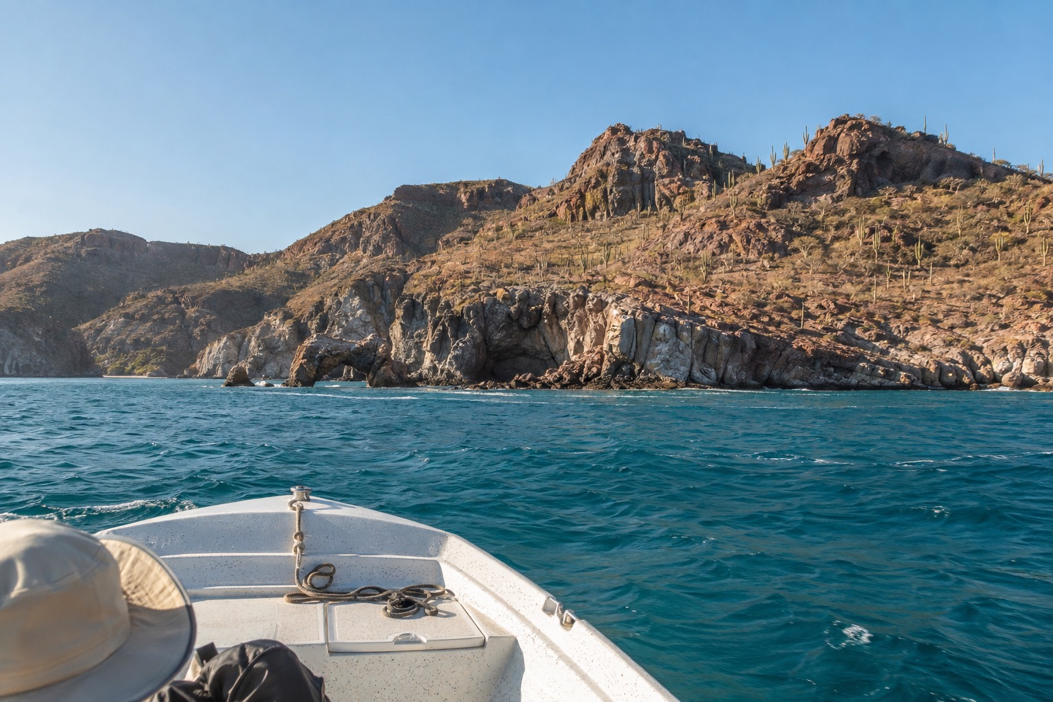 A small motorboat crossing open turquoise water toward a rocky desert island in the Bay of La Paz