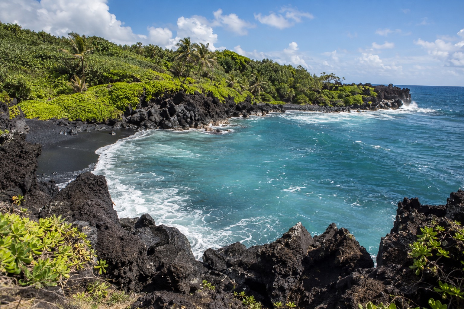 Black volcanic rock framing a small cove at Waianapanapa State Park on Maui's Hana coast