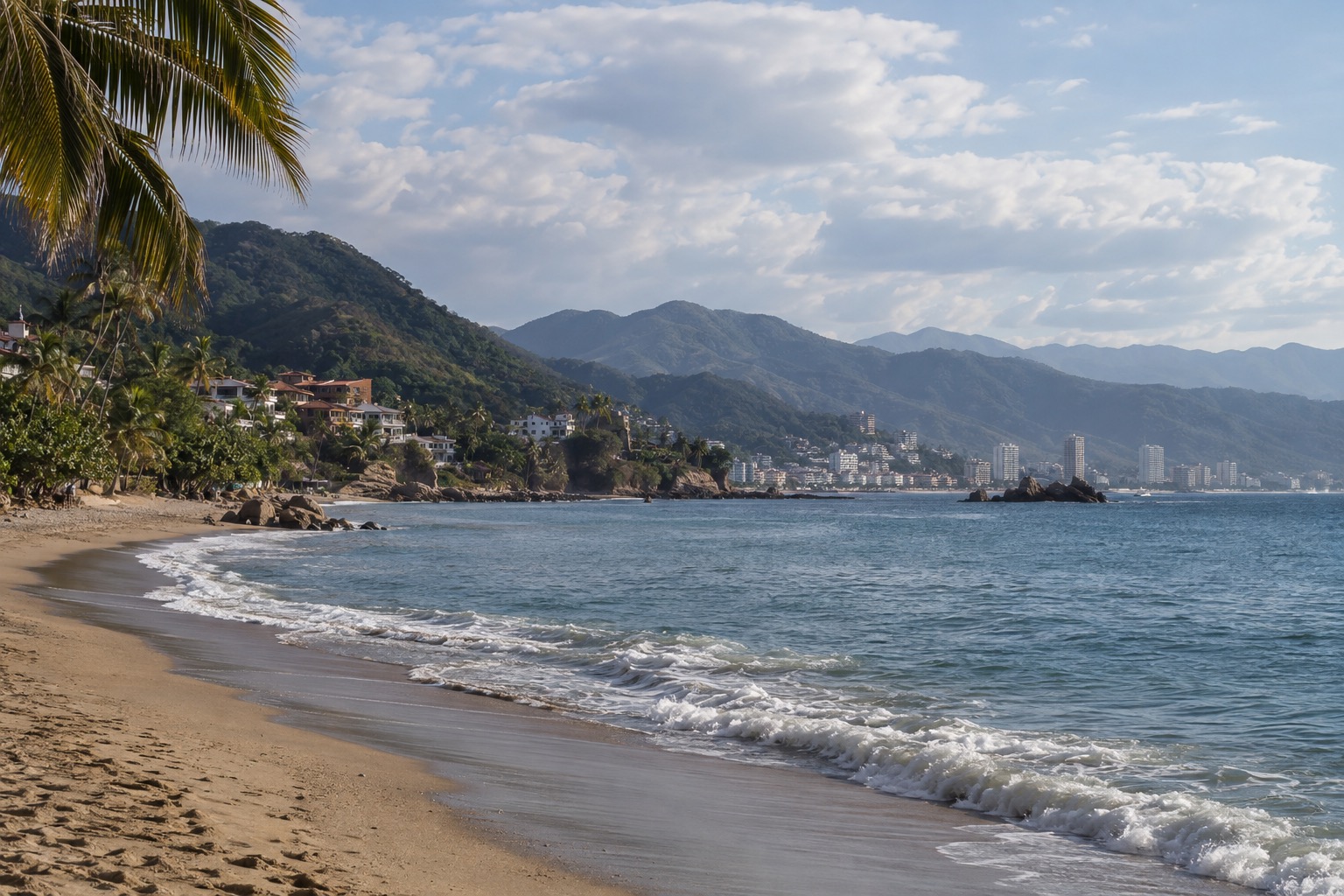 A wide sandy beach curving around a calm blue bay under scattered clouds, with a city skyline in the distance