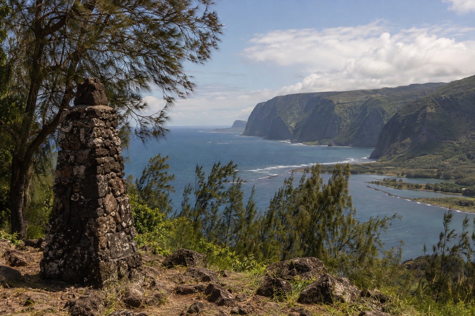 Stone monument and pine trees at an overlook above a distant coastal peninsula