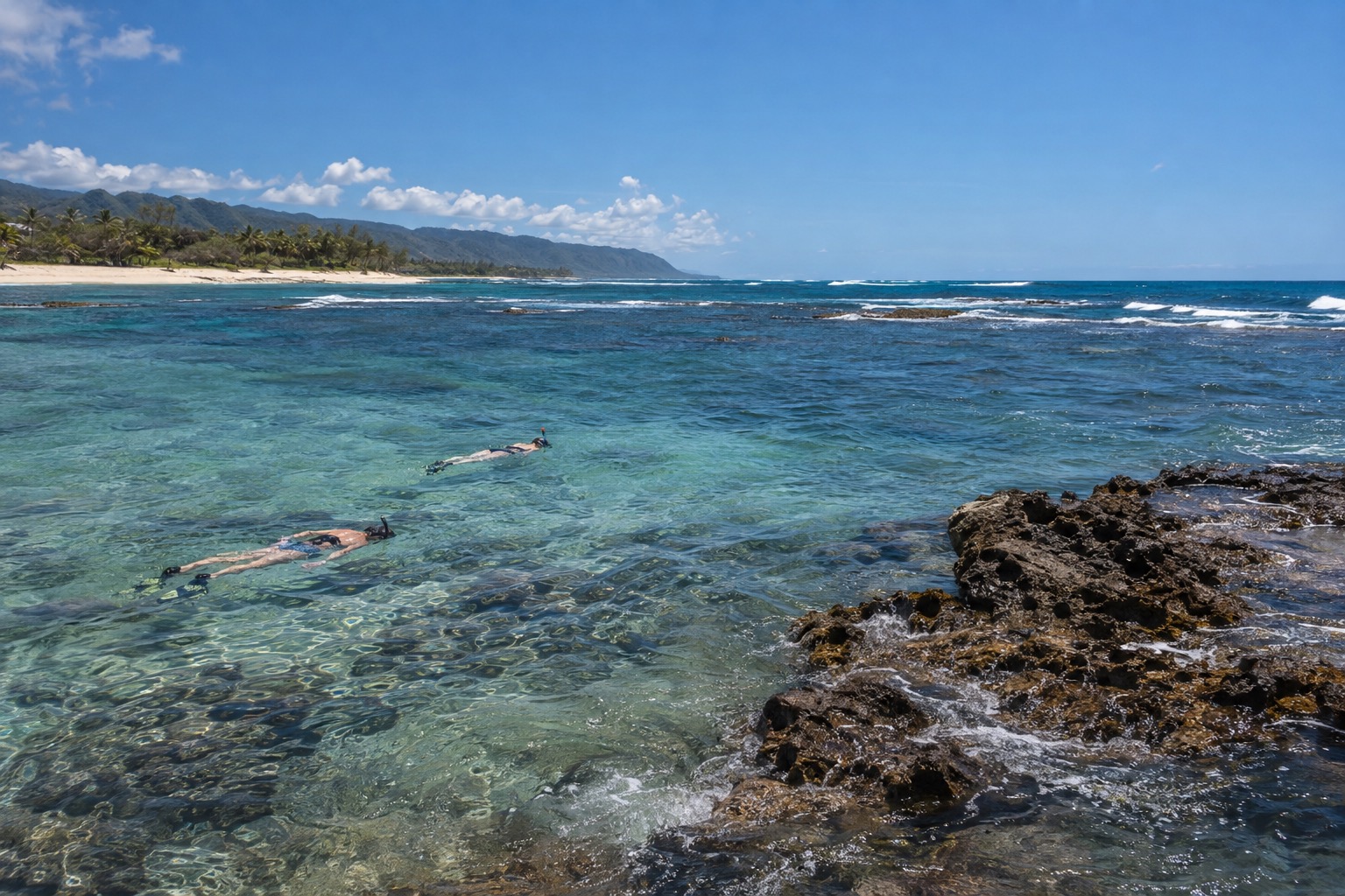 Snorkelers swimming near a rocky reef in shallow blue water