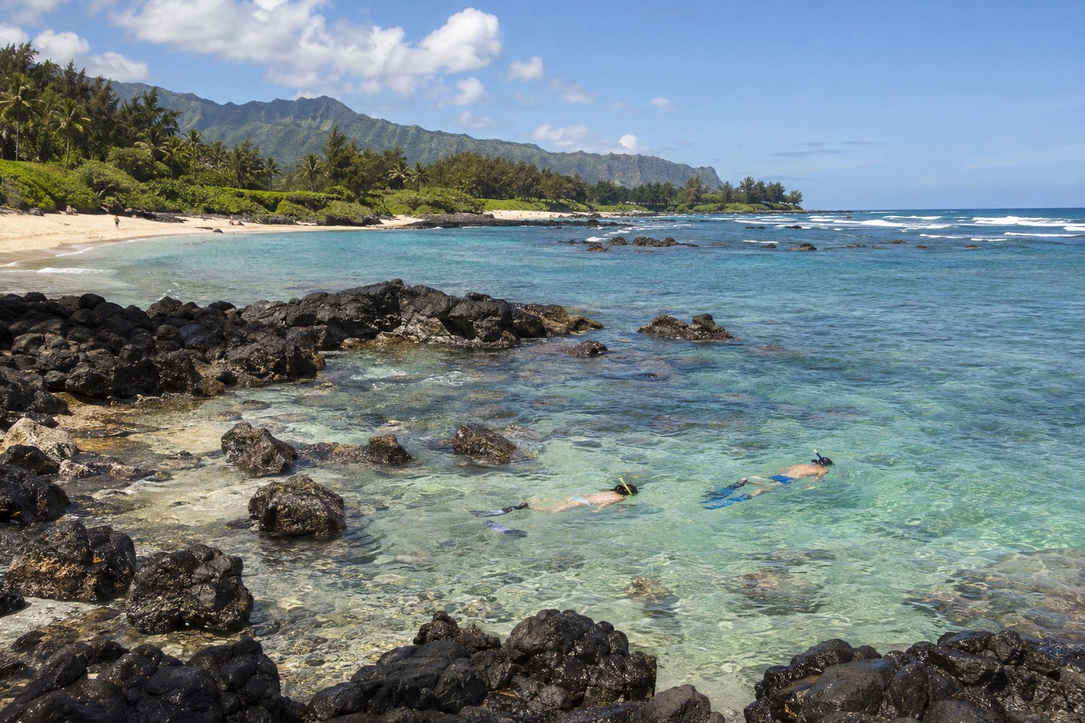 A rocky shoreline cove with calm shallow water and snorkelers near the shore