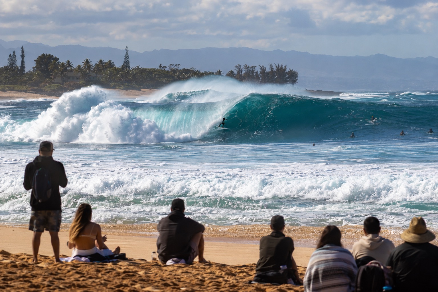 Large winter waves breaking at a North Shore surf break with spectators watching from the sand